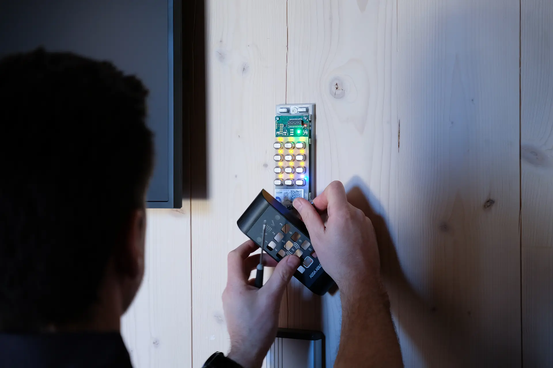 En person installerar ett digitalt kodlås på en trävägg